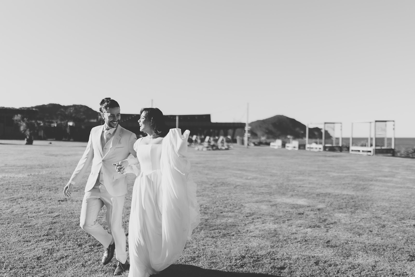 Casal recém-casado caminhando no gramado, com os morros da Praia do Rosa ao fundo